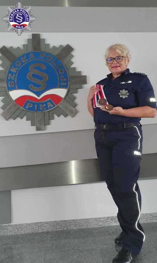 Umundurowana funkcjonariuszka stoi na tle logo Szkoły Policji prezentując zdobyte medale