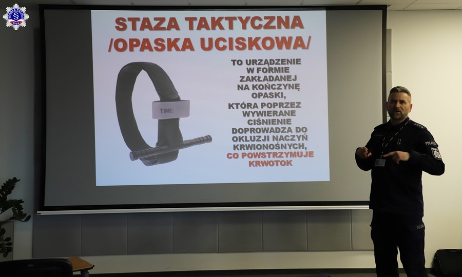 Umundurowany nadkom. Marcin Kolasiński podczas omawiania slajdu z opaską uciskową