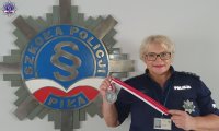 Policjantka prezentuje medal na tle logo Szkoły Policji w Pile