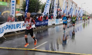 Biegacze na trasie półmaratonu w deszczowej pogodzie. W tle dopingujący mieszkańcy Piły z parasolami.