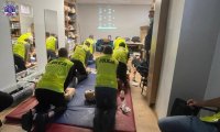 Grupa osób w kamizelkach odblaskowych z napisem POLICJA podczas zajęć z zakresu udzielania pierwszej pomocy medycznej ćwiczą resuscytację krążeniową oddechową.