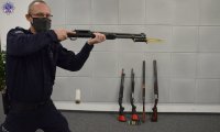 Umundurowany policjant w postawie strzeleckiej z bronią palną z zamontowanym przy wylocie lufy nożem taktycznym.