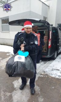 Umundurowany policjant w czapce świętego Mikołaja niesie worek z prezentami.