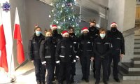 Grupa umundurowanych policjantek i policjantów w czapkach świętego Mikołaja stoją w holu głównym Szkoły Policji w Pile.