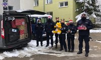 Grupa umundurowanych policjantów w czapkach świętego Mikołaja stojąca przy samochodzie w którym znajdują się prezenty i paczki dla dzieci