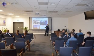 Nauczyciel policyjny podczas podczas wykładu na auli akademika Szkoły Policji w Pile.  W tle prezentacja multimedialna.
