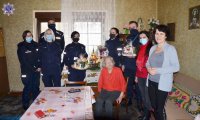 Grupa umundurowanych policjantów oraz trzy kobiety w mieszkaniu w trakcie spotkania i przekazania prezentów w ramach akcji Szlachetna Paczka.