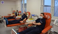 Trzech policjantów w maseczkach w pozycji pół siedzącej podczas pobierania krwi.