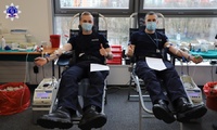 Dwóch policjantów siedzących na krześle medycznym  z podłączoną aparaturą do pobierania krwi.