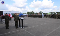 Dwóch żołnierzy przy mównicach oddający honor. W tle stojące drużyny klas mundurowych