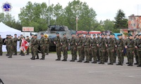 Poczet sztandarowy i stojący w szeregu żołnierze w zielonych beretach przepasani karabinami