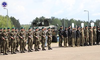 Stojący w szeregu żołnierze w zielonych beretach przepasani karabinami, obok uczniowie drużyn klas mundurowych, za nimi czołg