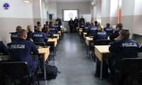 Zastępca Komendanta Szkoły Policji w Pile zwraca się w sali do policjantów w obecności przedstawicieli kadry dydaktycznej.