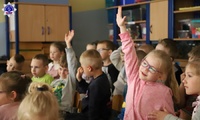 Przedszkolaki biorący aktywny udział w spotkaniu z podkom. Magdaleną Pałys podnoszą rękę do góry, aby zabrać głos