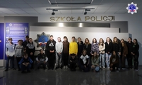 Zdjęcie grupowe wycieczki szkolnej zwiedzające Szkołę Policji w Pile. W tle logo Szkoły Policji.