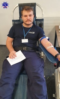 Mężczyzna z wąsem w policyjnym mundurze, siedząc na fotelu oddaje krew.