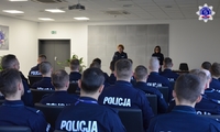 Absolwenci kursu specjalistycznego siedzący w auli akademika Szkoły Policji w Pile, na drugim planie kadra Szkoły.