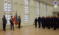 Poczet Sztandarowy wraz ze Sztandarem Szkoły Policji w Pile w umundurowaniu galowym oraz słuchacze Szkoły stojący w Auli Szkoły.